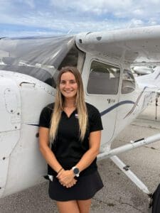 Brunette woman in black polo by single-engine plane